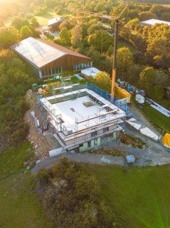 Aerial view of a construction site surrounded by forest and meadows with crane and building