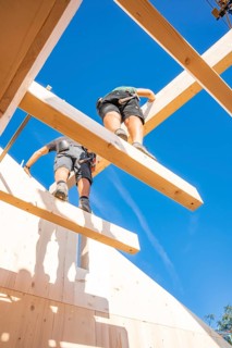 Two construction workers work on wooden scaffolding under a blue sky, Holzhausbau, Gechingen,