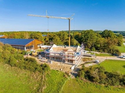 A construction site with a crane and a house under construction, surrounded by green nature and