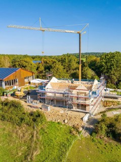 Building construction with scaffolding and crane in green surroundings, timber house construction,