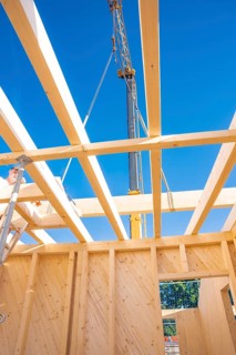 Wooden beams and a crane under a bright blue sky in a construction site, timber house construction,