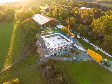 Construction site with a concrete foundation in a rural area, surrounded by green spaces, timber