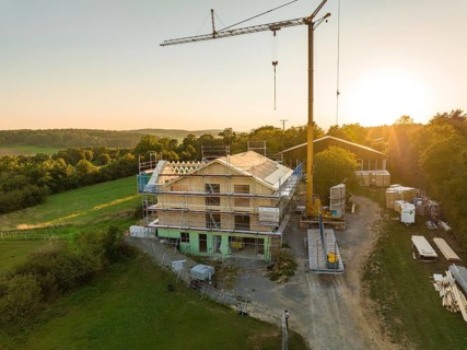 Building under construction, with a crane and scaffolding, in a green setting at sunset, timber