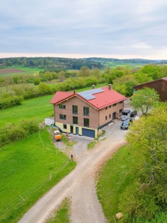 House with red roof and solar panel in rural area with green pastures and a road, Holzhausbau,