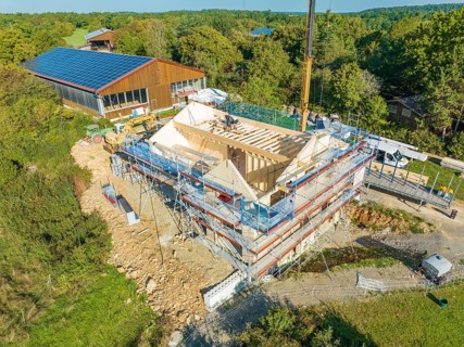 Bird's eye view of a construction site in a natural environment with solar building nearby, timber