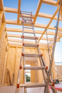 Interior view of a timber structure under construction, ladder leading upwards under blue sky,