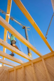 Construction worker balancing on wooden scaffolding under a clear sky, timber house construction,