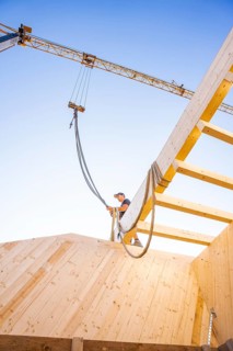 Timber structure under construction with a crane and a blue sky in the background, timber house