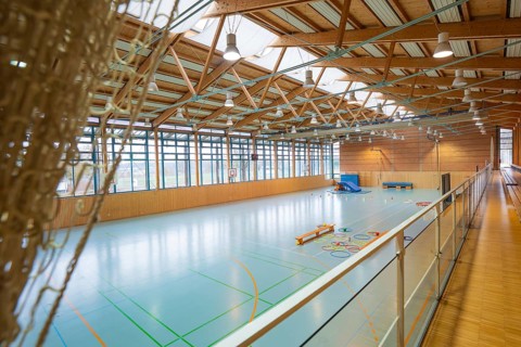 View of a spacious sports hall with basketball hoop and marked playing fields on the ground,