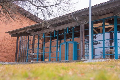 Modern architecture with large glass windows and wooden elements next to a wooded area, Schlehengäu