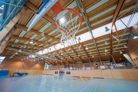 Basketball hoop in a large sports hall with wooden structure and floor markings, Schlehengäu