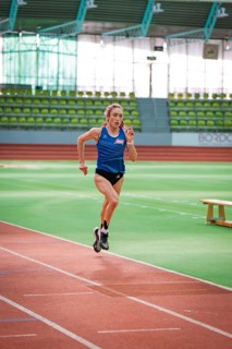 Woman running on a track in a stadium wearing a blue jersey, middle distance runner Katharina