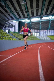Female athlete sprints energetically on a red track in a sports complex, middle distance runner