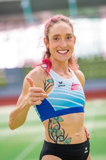 Woman showing thumbs up and smiling with tattoos in stadium, middle distance runner Katharina