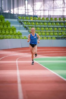 Woman sprinting straight ahead on a red track in the stadium, middle distance runner Katharina