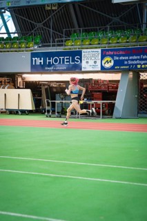 A sporty woman runs at high speed across the green track of a stadium with advertising, middle