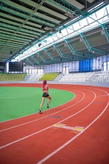 An athlete runs dynamically on a curvy red track in an indoor stadium, middle distance runner