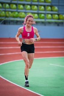 Determined, smiling woman running on an indoor track with visible enthusiasm, middle distance