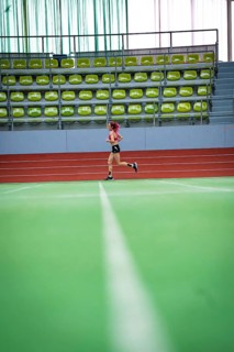 Female athlete running alone on an extensive track in a hall, middle distance runner Katharina