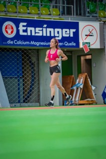 Female athlete running past a banner in a hall, middle distance runner Katharina Jaiser,