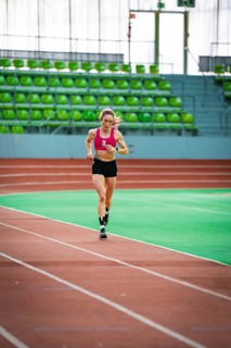 Sporty dressed woman running on an indoor track, showing speed and focus, middle distance runner