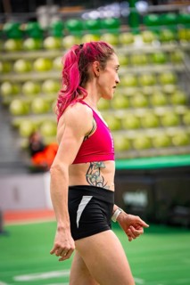 Side view of woman in sporty clothing, concentrated, with pink hair and tattoo, middle distance