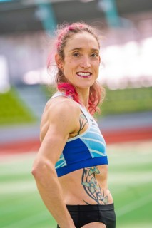 Sportswoman with blue sports outfit and tattoo in stadium, smiling with pink hair, middle distance