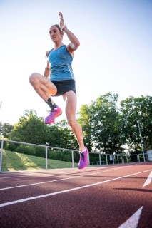 A sporty person jumps with momentum on the track in a blue outfit and pink shoes, middle distance
