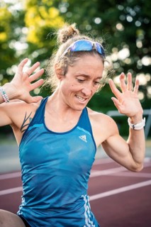 A happy runner in a blue sports outfit raises her hands with joy on the track, middle distance