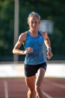 A focused runner on a racetrack wearing a blue sports outfit in sunshine, middle distance runner