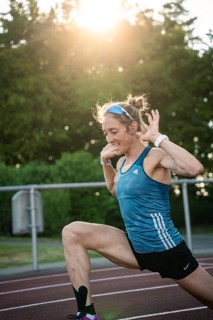 Woman stretching on the track at sunset, concentrated and energetic, middle distance runner