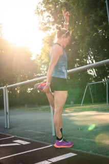 Woman standing on a running track while stretching, raised in sunlight, middle distance runner
