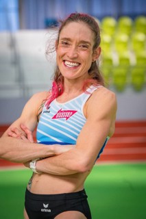 Self-confident sportswoman with pink hair in stadium, smiling friendly, middle distance runner