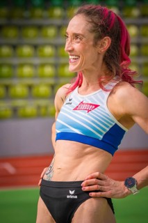 Smiling sportswoman with pink hair and tattoo, looks determined in the stadium, middle distance
