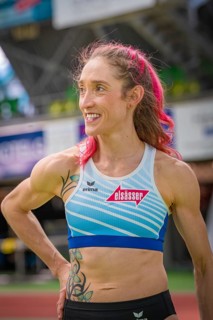 Smiling sportswoman with pink hair and blue sportswear in stadium, middle distance runner Katharina