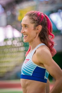 Happy sportswoman with pink hair in the stadium. Smiles and looks satisfied, middle distance runner