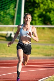 Woman running with energy on a sports track in green surroundings, middle distance runner Katharina