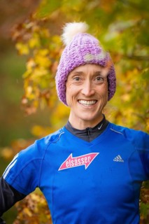 Woman wearing purple hat and blue sweater smiling in autumn surroundings, middle distance runner