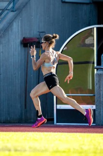 A woman in sporty clothes runs fast on a track in a stadium, middle distance runner Katharina
