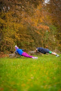 Two people doing push-ups on rocks in an autumnal forest, middle distance runner Katharina Jaiser,