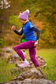 Woman in sporty clothing climbs energetically on rocks in autumn nature, middle distance runner