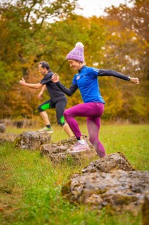 Two people jumping during dynamic training on rocks in autumn forest, middle distance runner