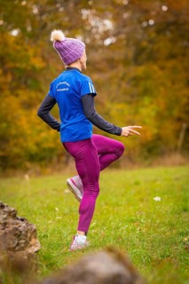 Woman wearing pink sports pants and blue jacket training in autumn forest, middle distance runner