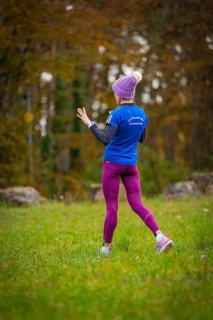 Woman in sporty clothes running in the forest surrounded by autumn trees, middle distance runner