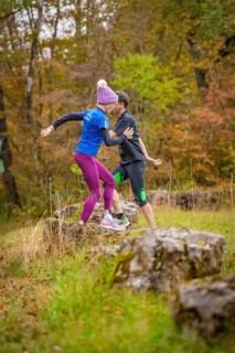 Two people train in the forest on rocks in an autumnal atmosphere, middle distance runner Katharina