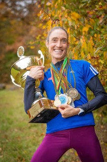 Radiant woman holding a big trophy and many medals in an autumn atmosphere, middle distance runner