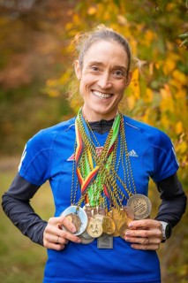 Woman with many medals around her neck smiling in autumn scenery, middle distance runner Katharina
