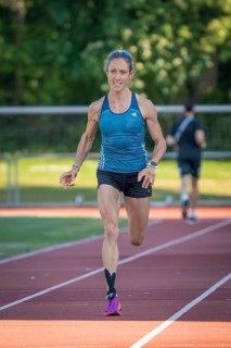 Athlete runs purposefully on the track in green, sunny surroundings, middle distance runner