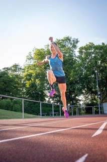 Athlete jumping on a track surrounded by green trees and bright sunshine, middle distance runner