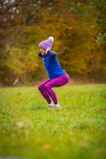 Woman wearing colorful sportswear doing jumping exercises on an autumnal meadow, middle distance